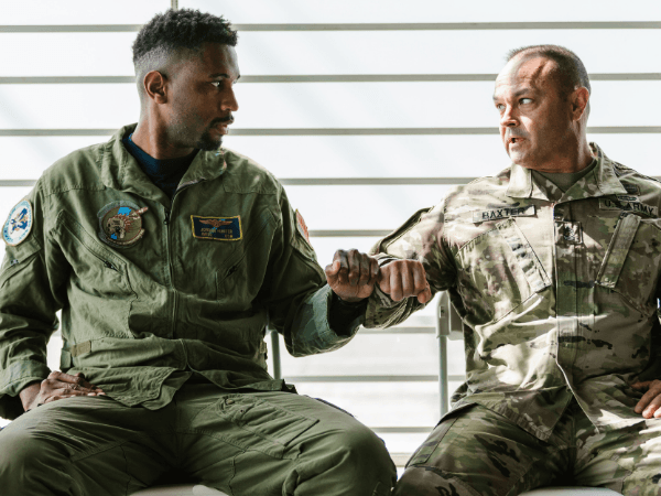 Two men sitting in military uniforms fist bumping