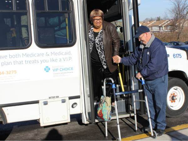 Woman exiting a small white transit bus with the help of an older man